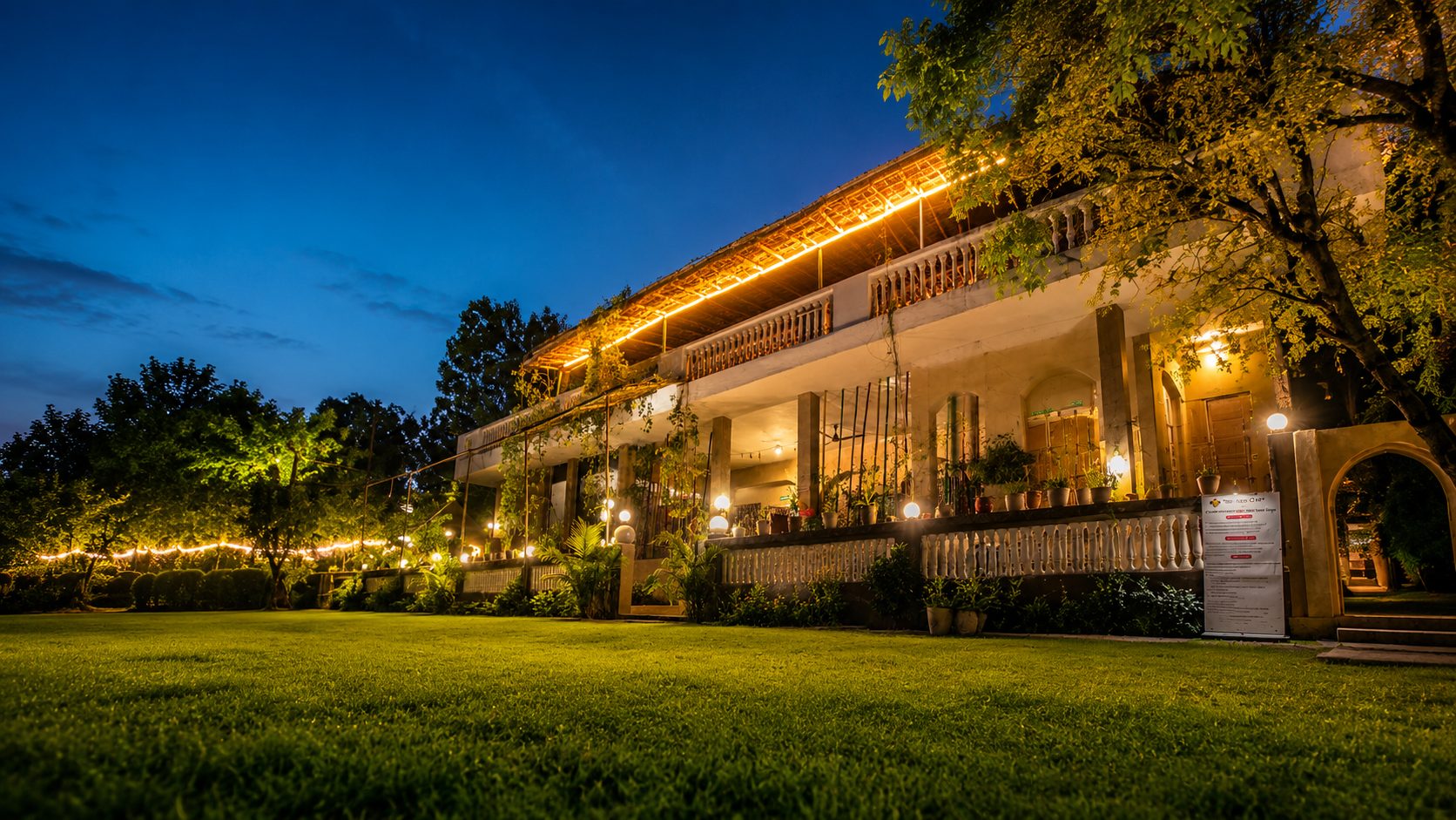 The DNA Camp property at dusk — thatched building, lit lawns and fairy lights under a twilight sky